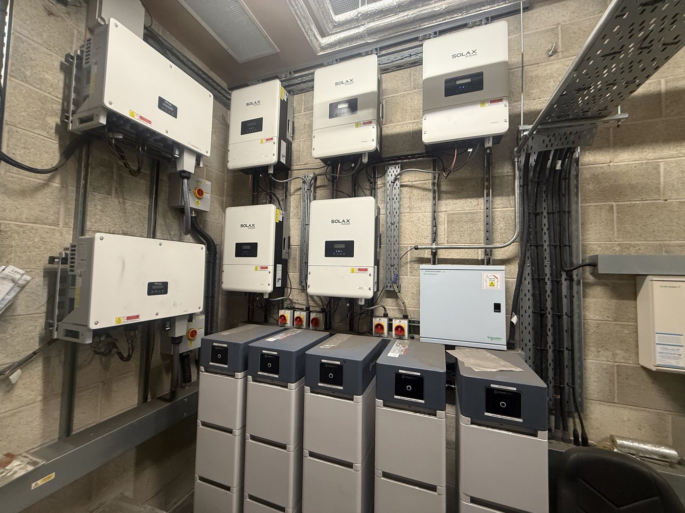 A commercial plant room with a row of wall-mounted SolaX storage inverters and a stack of battery modules — a multi-inverter commercial solar-plus-storage system, several inverters of which were sitting idle or in error.